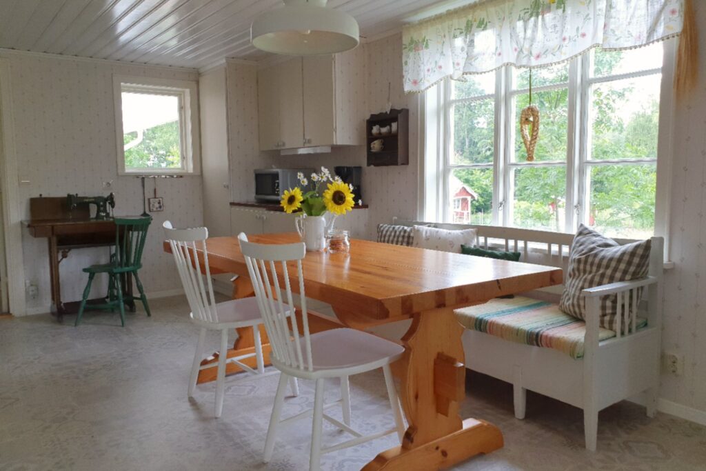 Ljust kök och matplats i Farm med träbord, fönster och utsikt mot trädgården