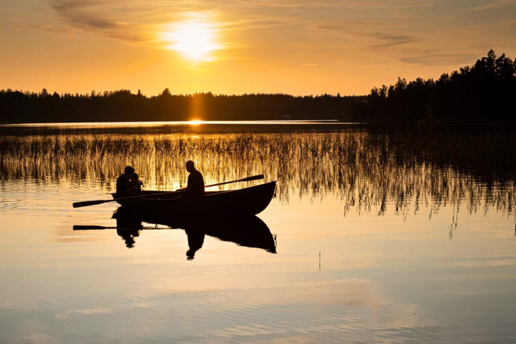 Gäste im Ruderboot bei Sonnenuntergang auf dem See bei Snokebo Gård in Småland
