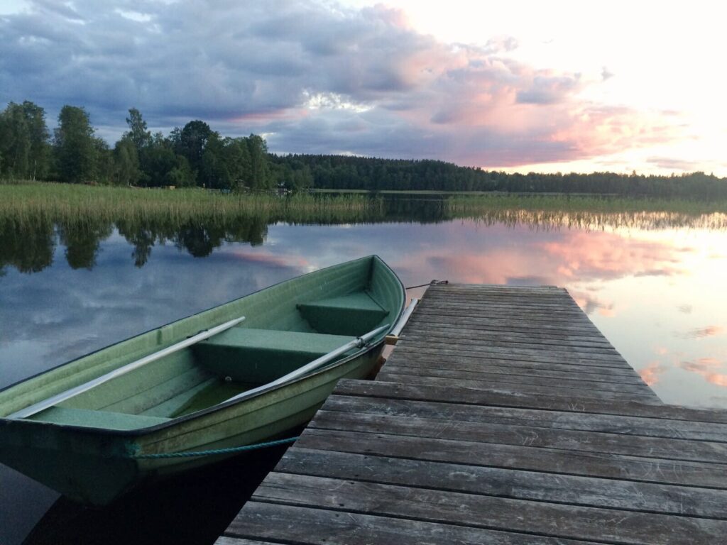 Roddbåt vid brygga på lugn sjö i kvällsljus