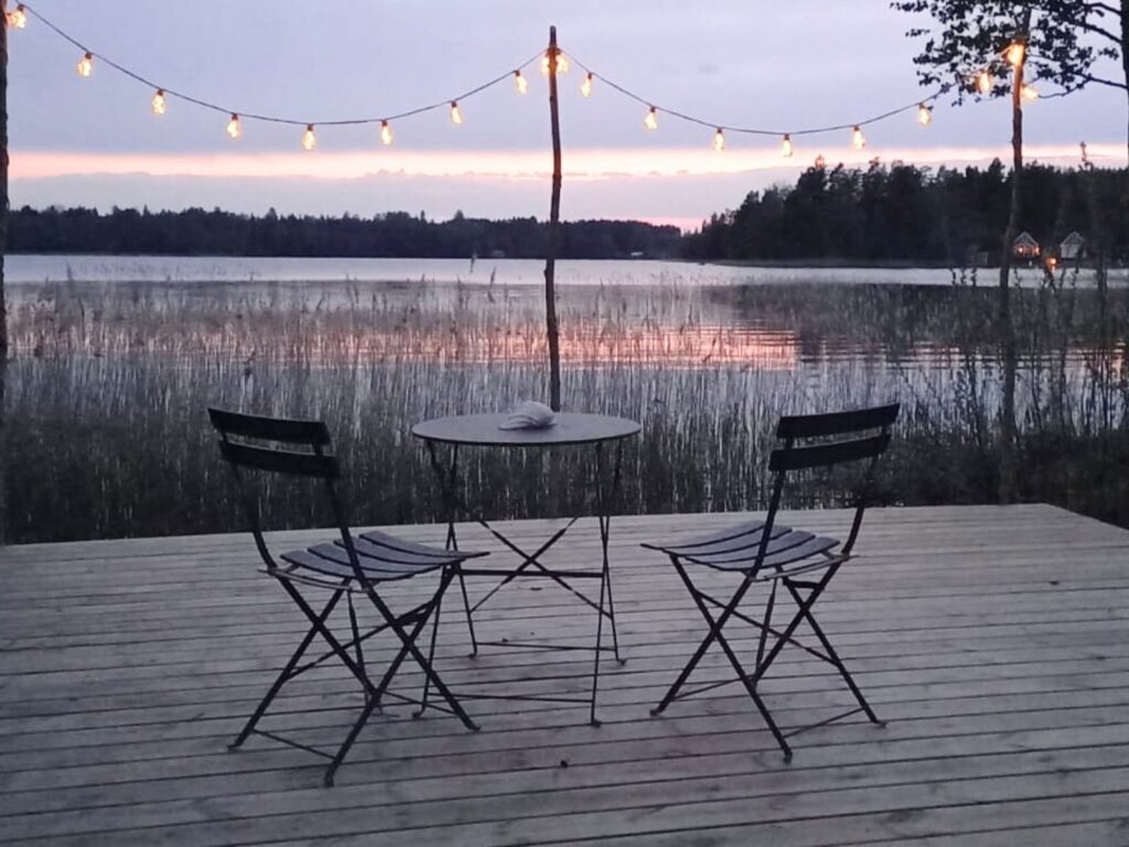 Utsikt över sjön från en träveranda med bord och stolar i kvällsljus.