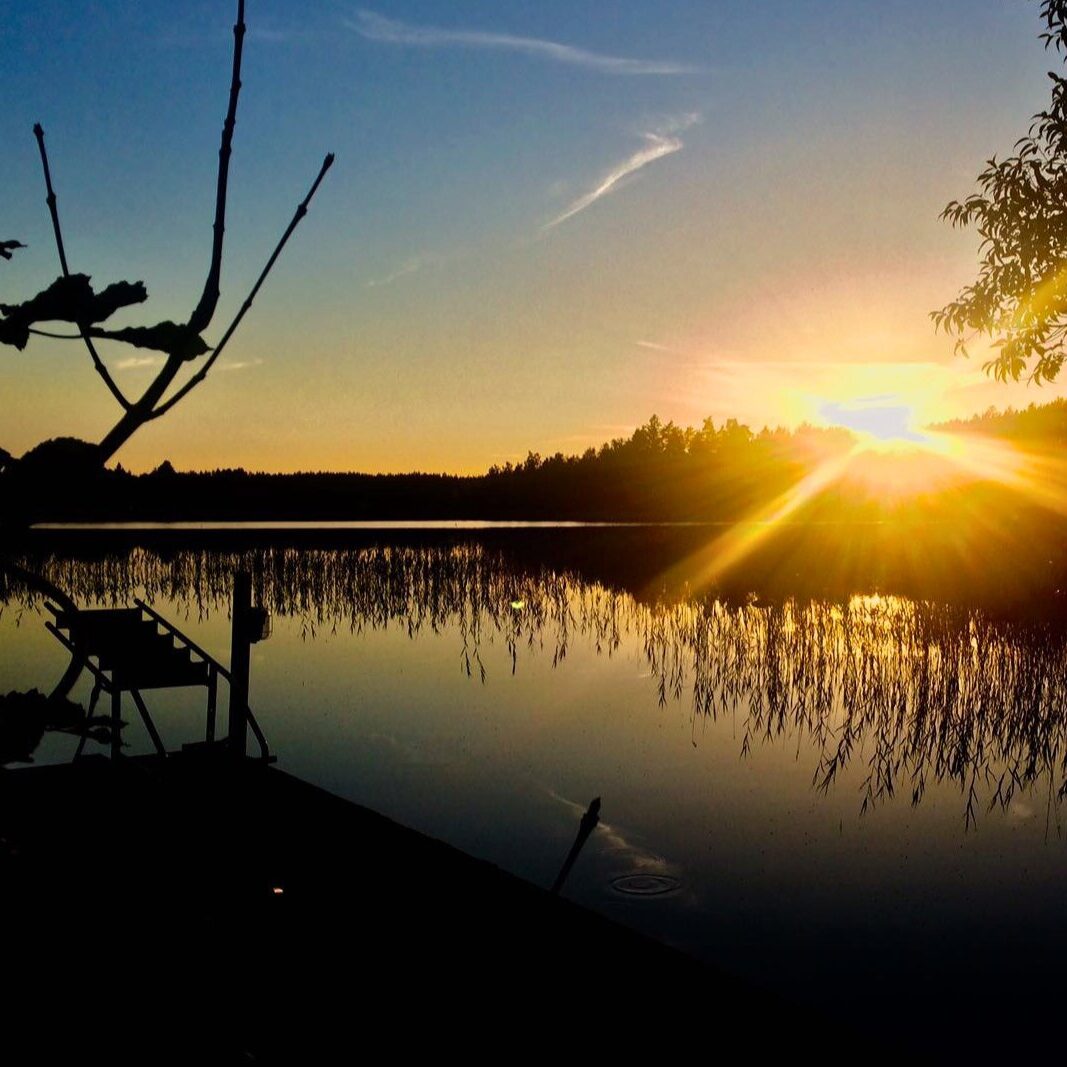 Solnedgång över sjön vid Snokebo Gård en sommarkväll, med brygga och stilla vatten